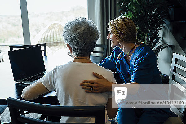Hausangestellte diskutiert am Laptop mit älterer Frau am Esstisch