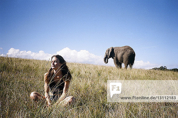 Nachdenkliche Frau sitzt auf Landschaft mit Elefant im Hintergrund
