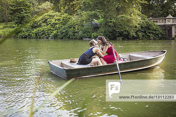 Lesbian couple kissing while sitting in boat amidst lake