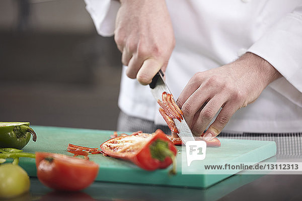 Mitschnitt eines Küchenchefs beim Zerkleinern von rotem Jalapeno-Pfeffer auf einem Schneidebrett in einer Großküche