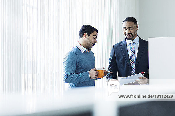 Businessmen discussing over document while standing in brightly lit office