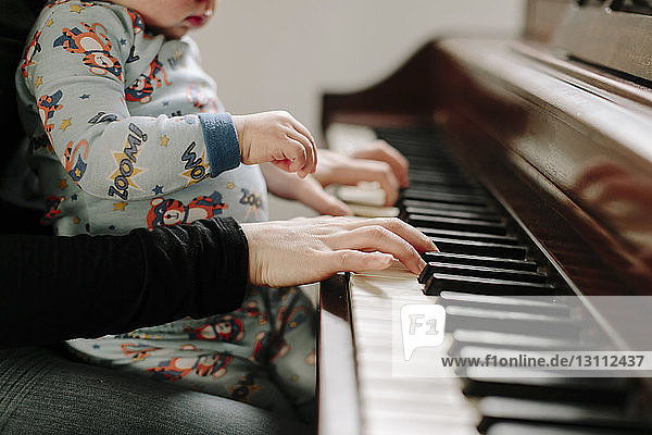 Midsection of mother with son playing piano at home