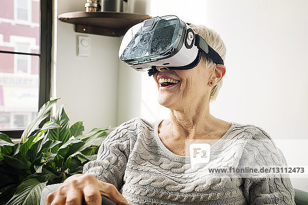 Glückliche ältere Frau trägt zu Hause einen Virtual-Reality-Simulator an der Wand