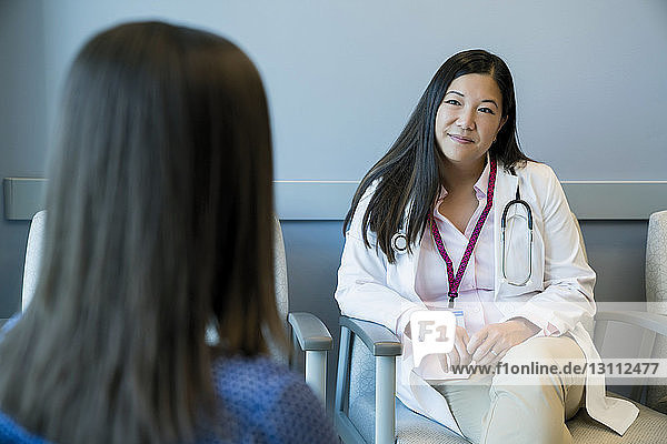 Female doctor looking at woman while sitting on chair in hospital waiting room