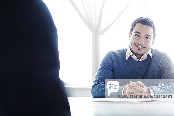 Smiling businessman sitting at table in brightly lit office