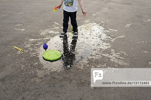 Niedriger Teil eines Jungen mit Spielzeug auf nasser Straße stehend