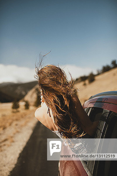 Unbeschwerte junge Frau mit zerzaustem Haar  die sich aus dem Autofenster lehnt
