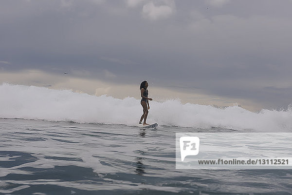 Seitenansicht einer Frau beim Surfen auf dem Meer vor bewölktem Himmel