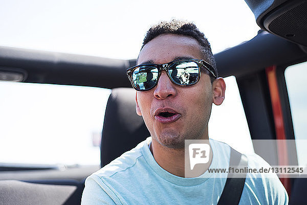Nahaufnahme eines Mannes  der eine Sonnenbrille trägt  während er im Geländewagen gegen den Himmel fährt