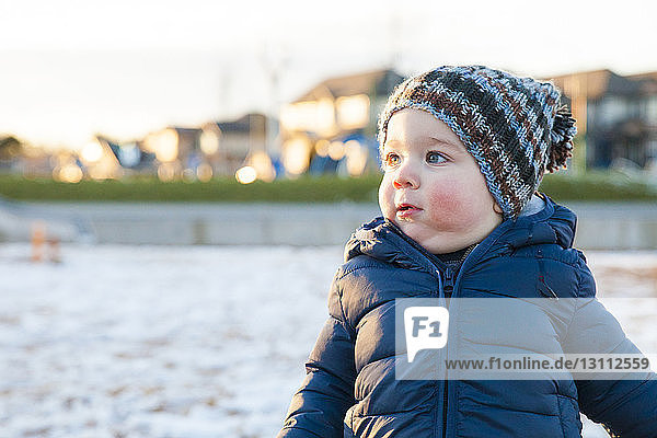 Cute boy looking away while standing at playground during winter