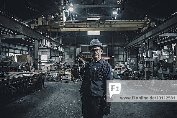 Porträt eines männlichen Arbeiters der ein Arbeitsgerät trägt während er in der Fabrik steht