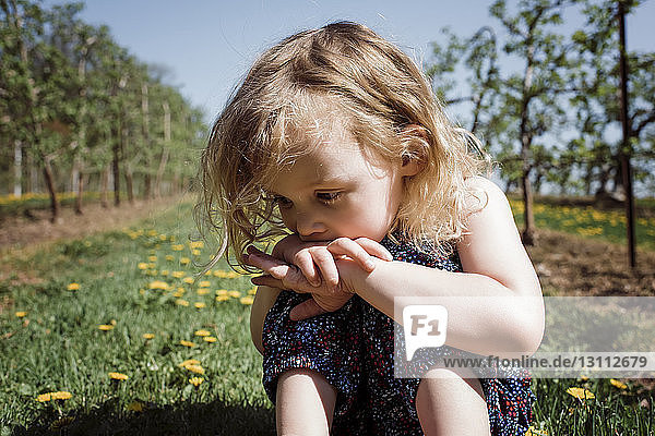 Close-up of cute thoughtful girl sitting on field during sunny day