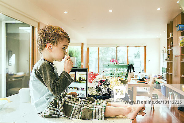 Side view of cute boy having drink while sitting on table in living room at home