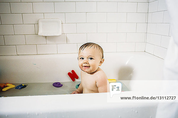 Porträt eines süßen Jungen  der in einer Badewanne vor einer gefliesten Wand badet