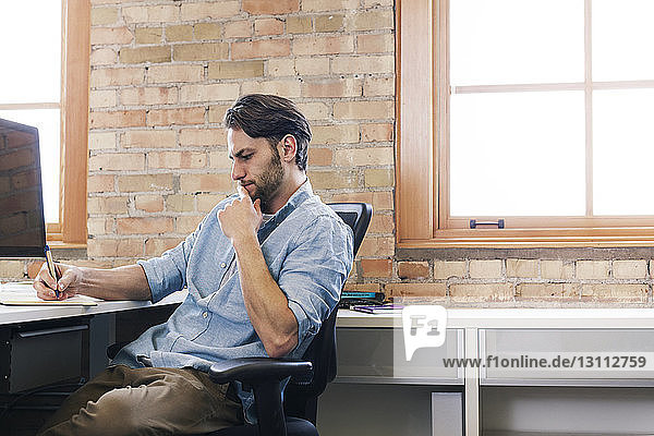 Businessman writing while working at desk in office