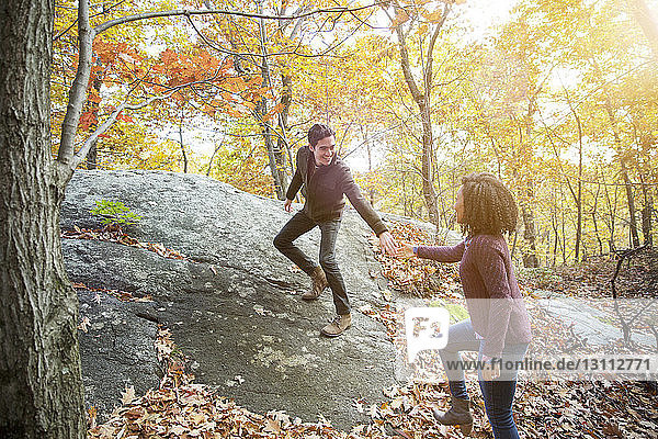 Mann hilft Freundin beim Gehen auf Fels im Wald