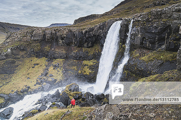 Hochwinkelaufnahme eines Mannes  der auf einem Hügel am Wasserfall steht