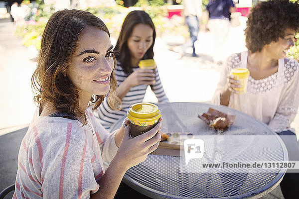 Friends holding coffee cup while sitting at sidewalk cafe