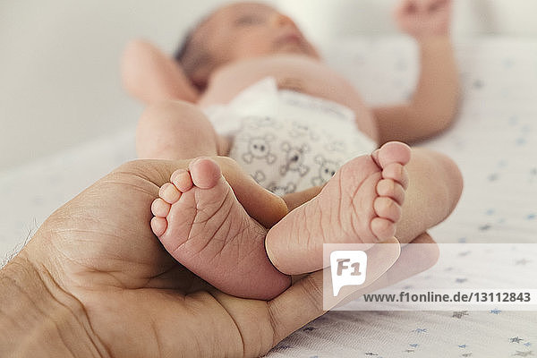 Ausgeschnittenes Bild einer Person  die die Füße des Babys auf dem Bett hält