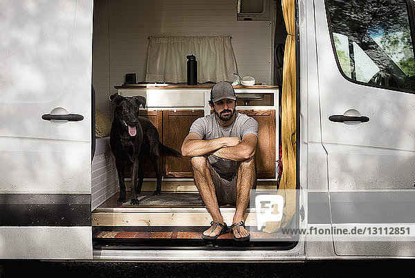 Nachdenklicher Mann mit verschränkten Armen sitzt mit Hund im Wohnmobil