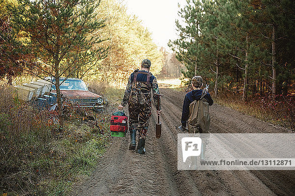 Rear view of father with son walking on dirt road in forest