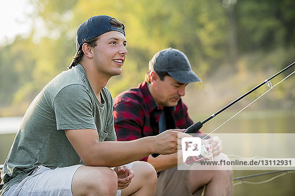 Male friends fishing while sitting at lakeshore