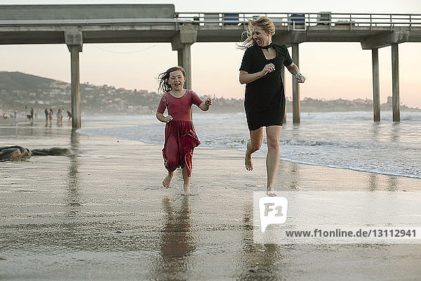 Playful mother and daughter running at beach