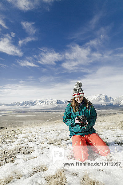 Wanderin schaut in die Kamera  während sie auf verschneitem Feld vor den Bergen kniet