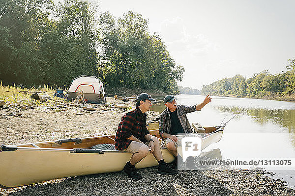 Männliche Freunde unterhalten sich  während sie auf einem Boot auf einem Campingplatz am See sitzen