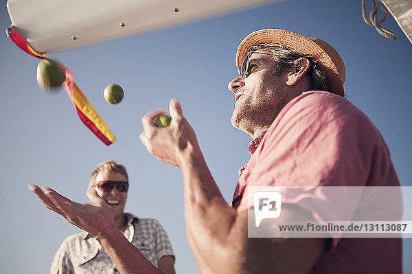 Low angle view of man playing with lemons against sky
