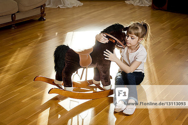 Mädchen umarmt Schaukelpferd  während sie auf dem Boden sitzt