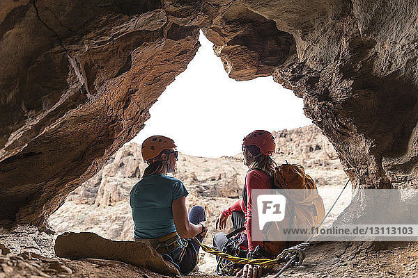 Female hikers sitting on entrance of cave in rock formation
