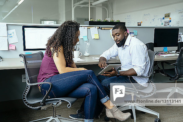 Geschäftsleute diskutieren über einen Tablet-Computer  während sie im Büro am Schreibtisch sitzen