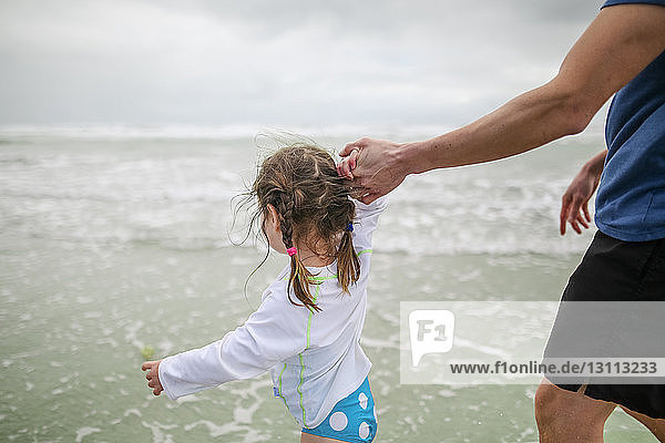 Daughter holding father's hand while walking in sea