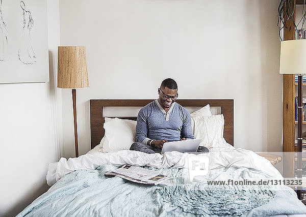 man using laptop while sitting on bed at home