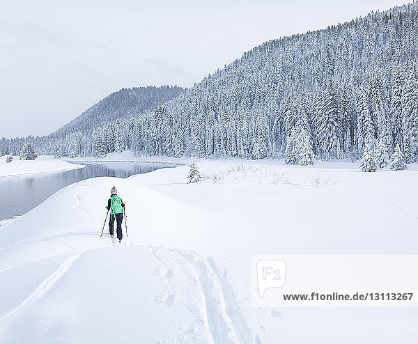 Rückansicht einer Wanderin  die auf einem schneebedeckten Feld gegen den Himmel wandert