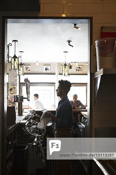 Seitenansicht des Eigentümers  der Gläser an der Bartheke von Kunden im Cafe reinigt