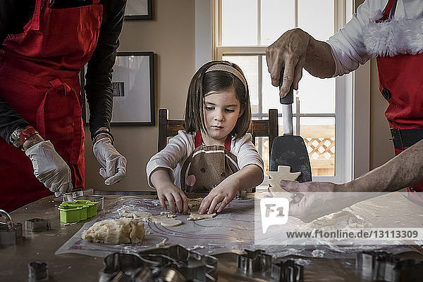 Granddaughter helping grandparents in making Christmas cookies on table at home