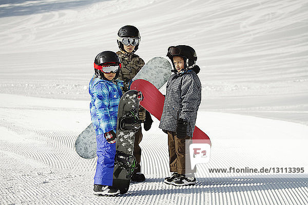 Geschwister tragen Snowboards  während sie auf einem schneebedeckten Feld stehen