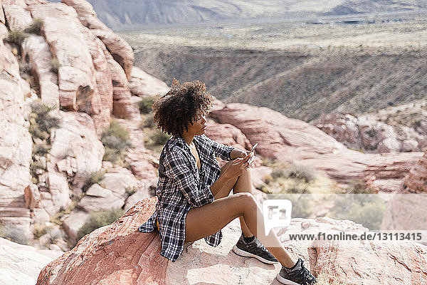 Hochwinkelaufnahme einer Frau  die ein Smartphone benutzt  während sie auf einer Felsformation sitzt