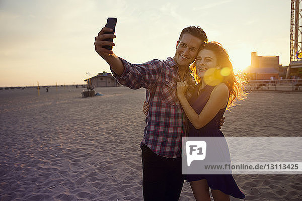 Young couple taking selfie while standing on sand during sunset