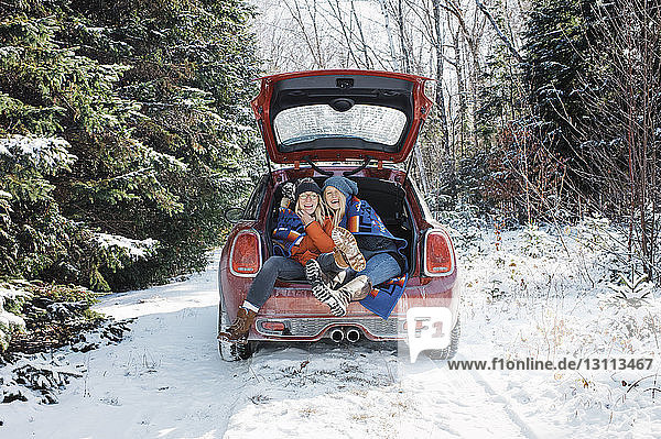Fröhliche Freundinnen sitzen im Winter im Kofferraum eines Autos im Algonquin-Provinzpark