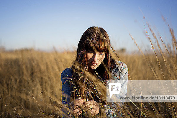 Nachdenkliche Frau sitzt auf dem Feld vor klarem Himmel