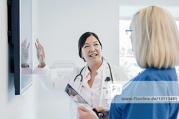 Ärztin gestikuliert am Flachbildschirm  während sie mit einer Kollegin im Krankenhaus diskutiert