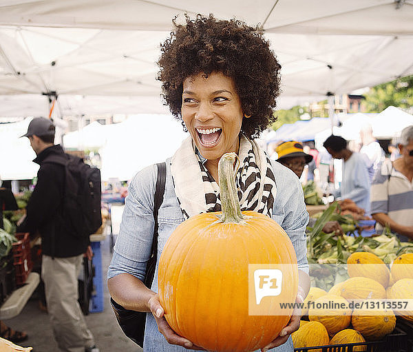 Happy woman with mouth open carrying pumpkin at market