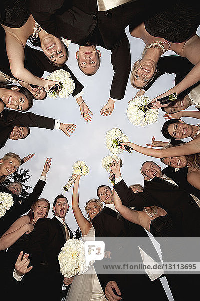 Directly below view of happy friends arms raised with bride and groom against sky