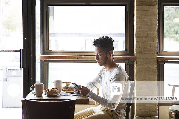 Junger Mann telefoniert bei Croissants und Kaffee im Café