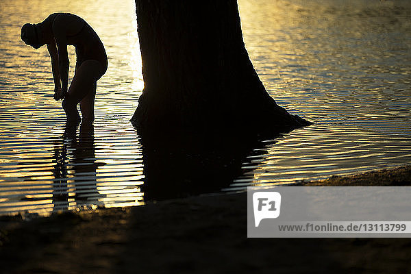 Scherenschnittschwimmer beugt sich bei Sonnenuntergang beim Training im See