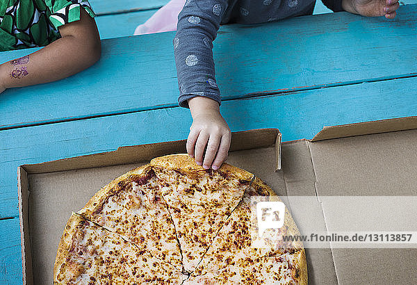 Draufsicht auf ein Mädchen  das ein Pizzastück auf dem Tisch hält