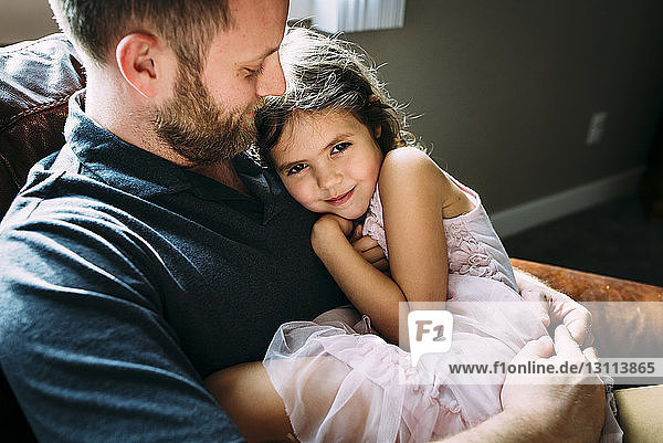 Porträt eines Mädchens mit Vater zu Hause auf dem Sofa sitzend